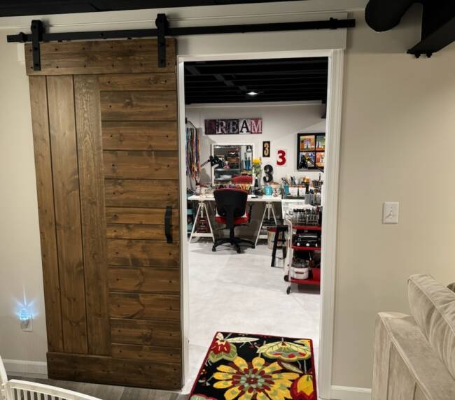 Room with a sliding wooden barn door, leading to a colorful craft room with a variety of supplies and decorations, and a floral rug on the floor