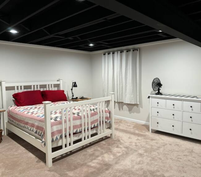 Bedroom with a white wooden bed frame, a patterned quilt, red pillows, and a white dresser