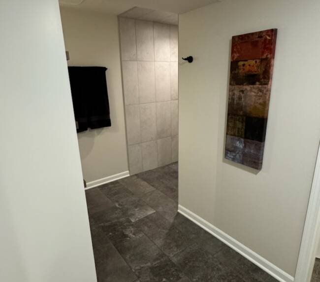 Bathroom with large light grey tiles in the shower area, dark grey floor tiles, and white walls