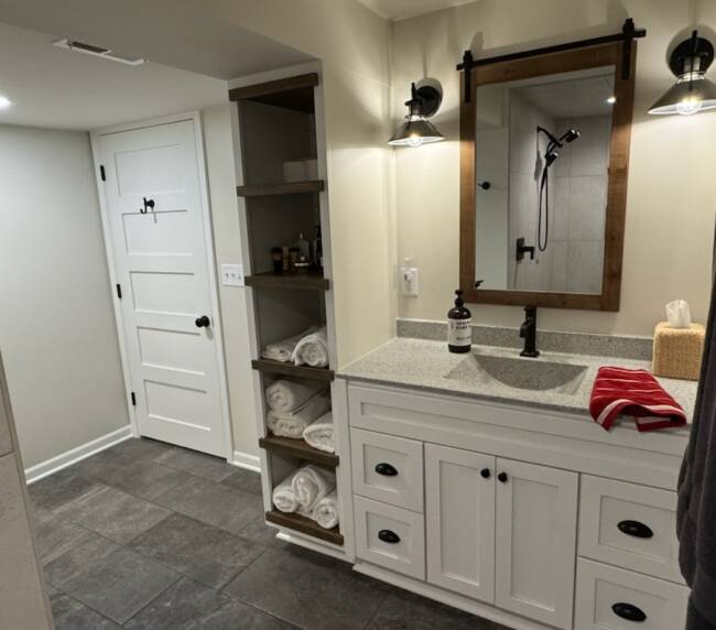 Bathroom with white cabinets, a light grey countertop, a wooden-framed mirror, and dark grey floor tiles