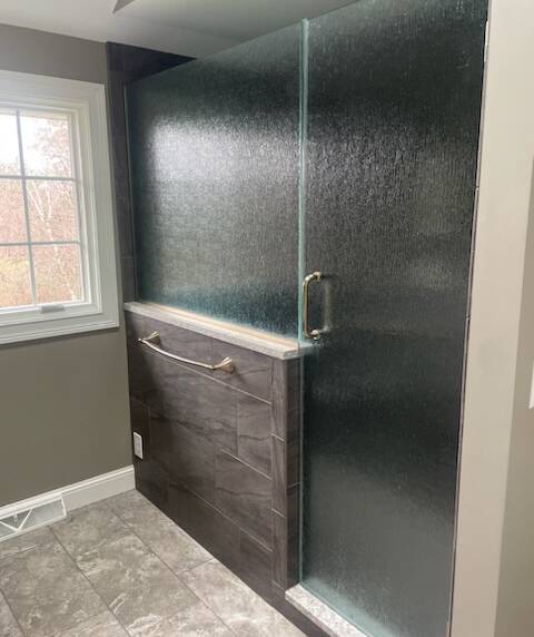 Shower with textured glass panels, dark gray tiles, and a marble ledge