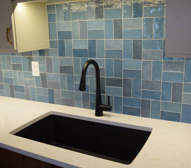 Modern kitchen sink with a black faucet, white countertop, and blue tile backsplash