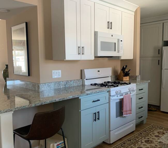 Kitchen with white cabinetry, granite countertops, a white microwave and stove, light blue lower cabinets, and a wooden floor