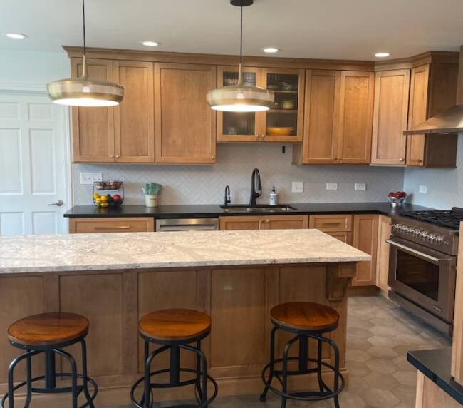 Kitchen with wooden cabinets, black countertops, and a large granite island. Features a herringbone backsplash, stainless steel appliances, and hexagonal tile flooring