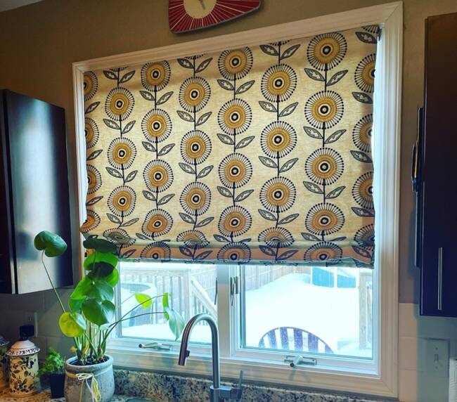 Kitchen window with a decorative floral-patterned Roman shade and granite countertop