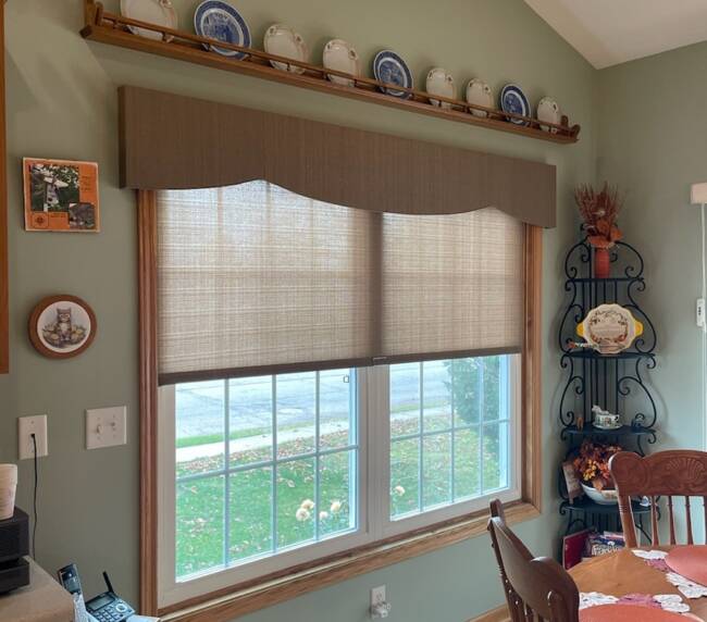 Kitchen area featuring a window with brown fabric valance and roller shades