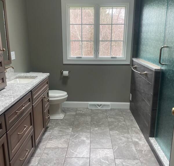 Bathroom with a large window, marble flooring, rich wooden vanity, and a textured glass shower