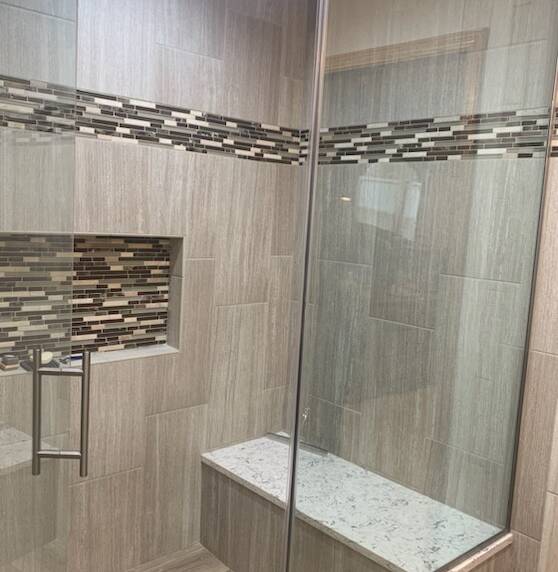 Shower with large beige tiles and a contrasting horizontal mosaic tile accent. Features a built-in niche and a granite bench
