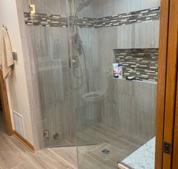 shower with beige tiles and a horizontal mosaic tile accent. Features a built-in niche and granite bench