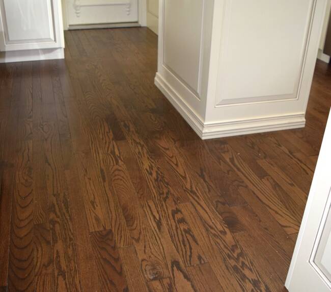 Dark wood plank flooring in a kitchen, leading towards a white door
