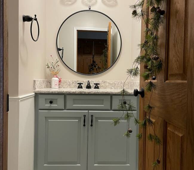 bathroom with a soft sage green vanity, a granite countertop, a round mirror, and flooring with a wood-look