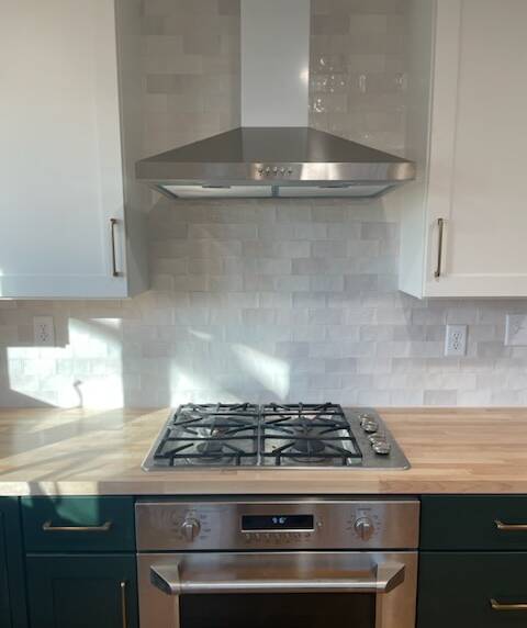 Kitchen with a stainless steel range and hood, white tile backsplash, and wooden countertops