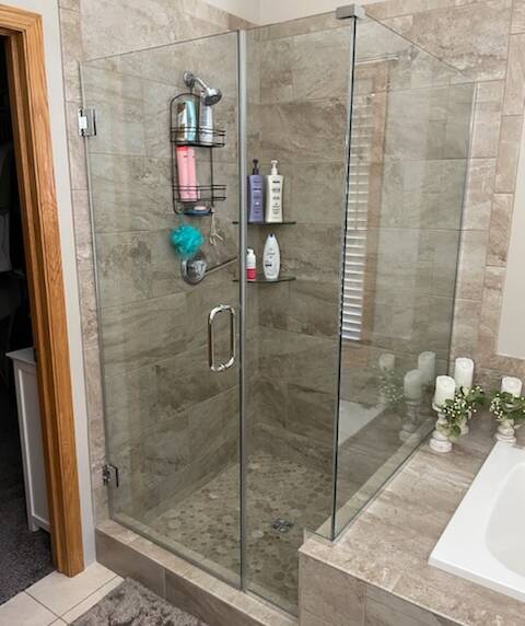Shower with large beige tiles and a glass enclosure. The shower floor features mosaic tiles