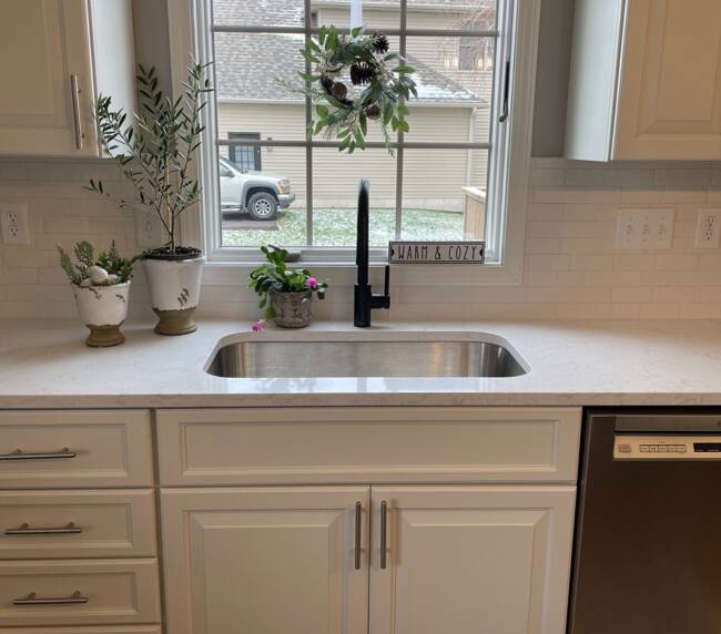 White kitchen with a stainless steel sink, black faucet, and white subway tile backsplash