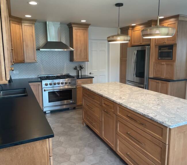 kitchen with wooden cabinetry, black countertops, and a large central island with granite top and a herringbone backsplash